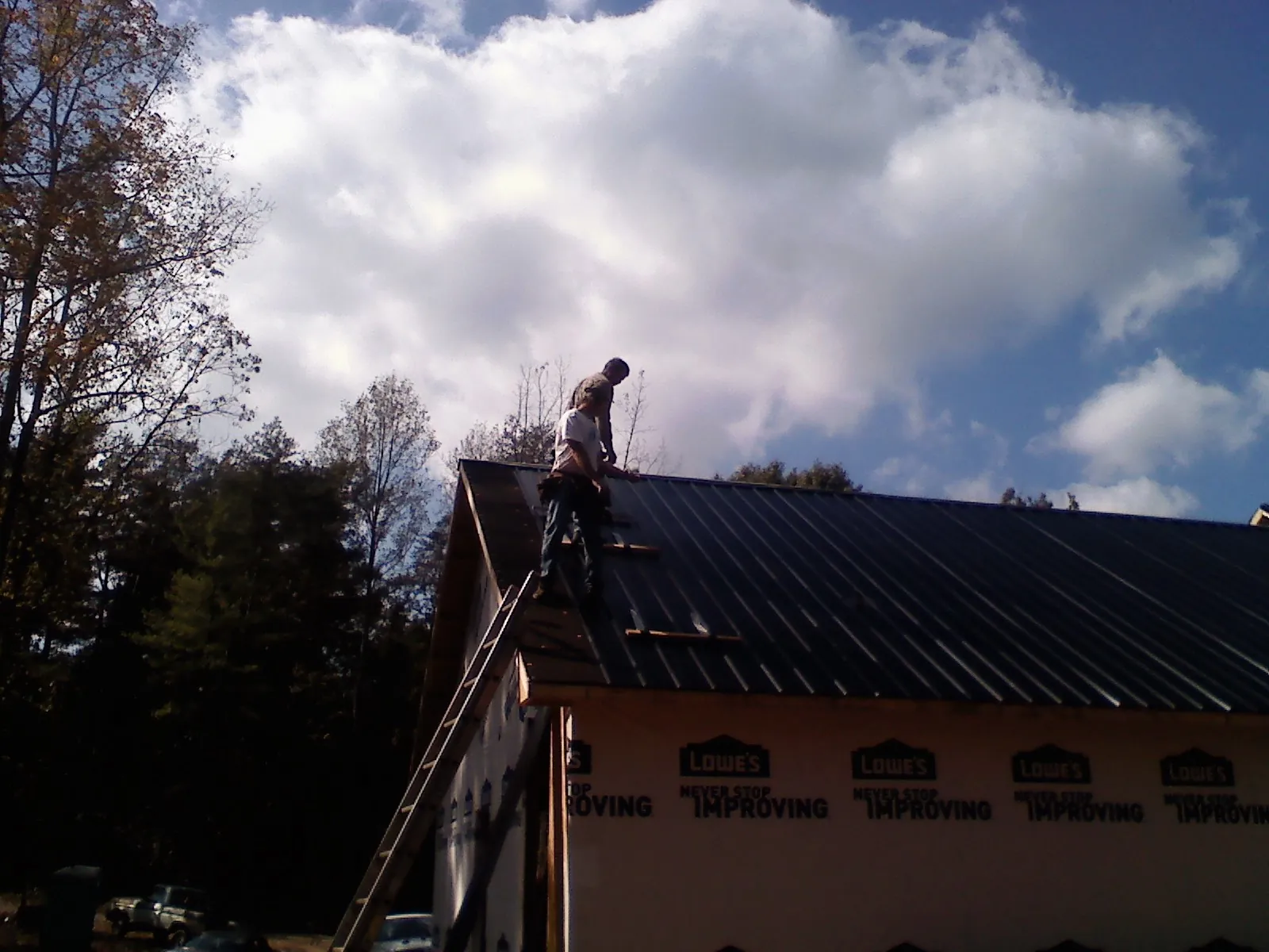 Roofer fastening dark metal panels high against a cloudy sky, from a Roof Inspection job in Bassett