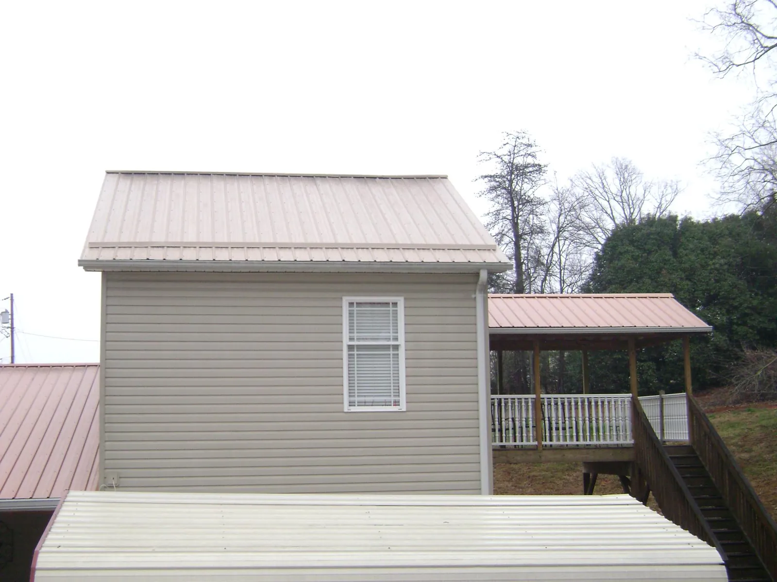 Tan metal roofs on a two story addition and attached porch, from a Roof Replacement job in Bassett